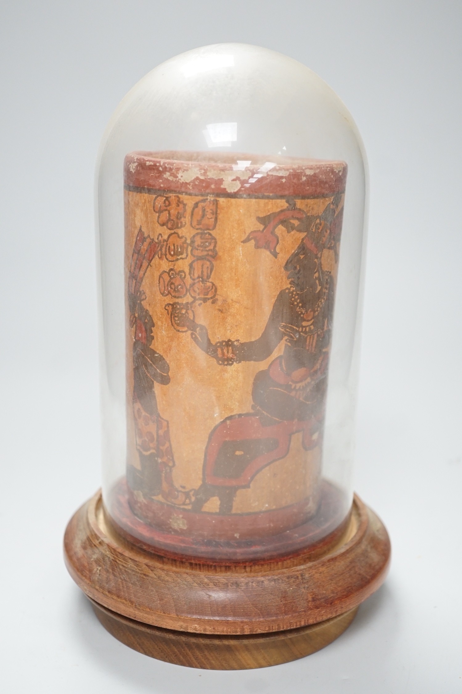 A Mayan pigment painted terracotta cylindrical vessel, possibly 7th-9th century AD., 17.2cm high, under a glass dome with revolving wood stand, total height 26cm